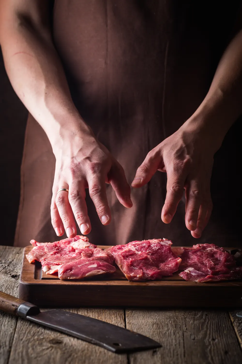 Mani sopra tagli di carne cruda su un tagliere di legno, con un coltello sul tavolo